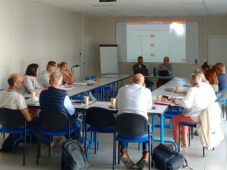 Groupe de personnes autour d'une table devant 2 intervenants