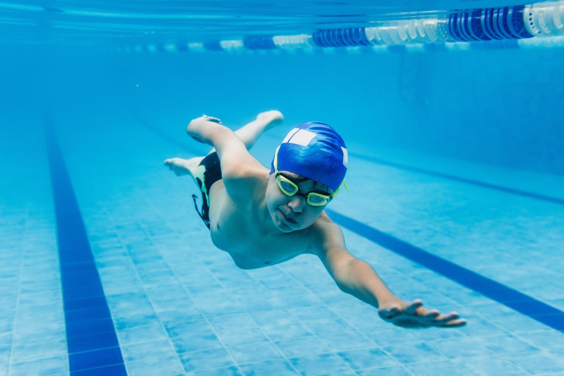 Enfant qui nage sous l'eau dans une piscine avec bonnet de bain et lunettes de plongée
