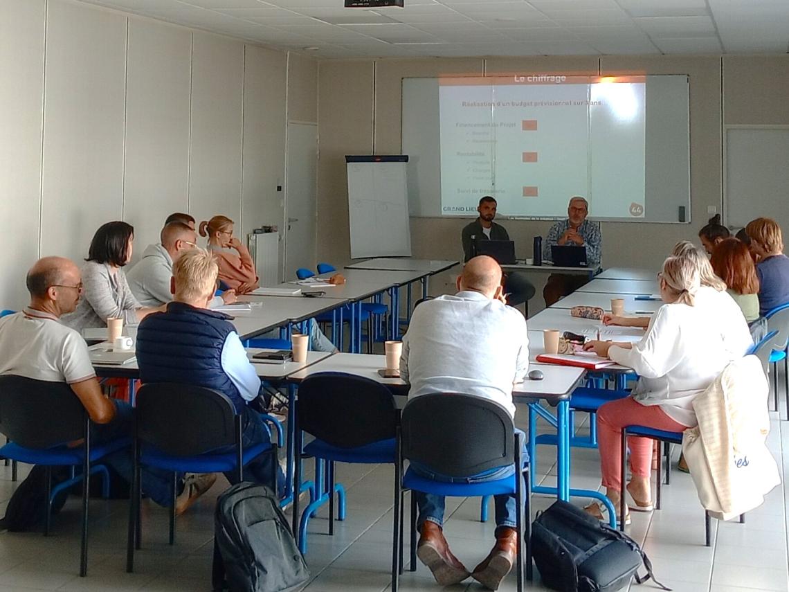 Groupe de personnes autour d'une table devant 2 intervenants